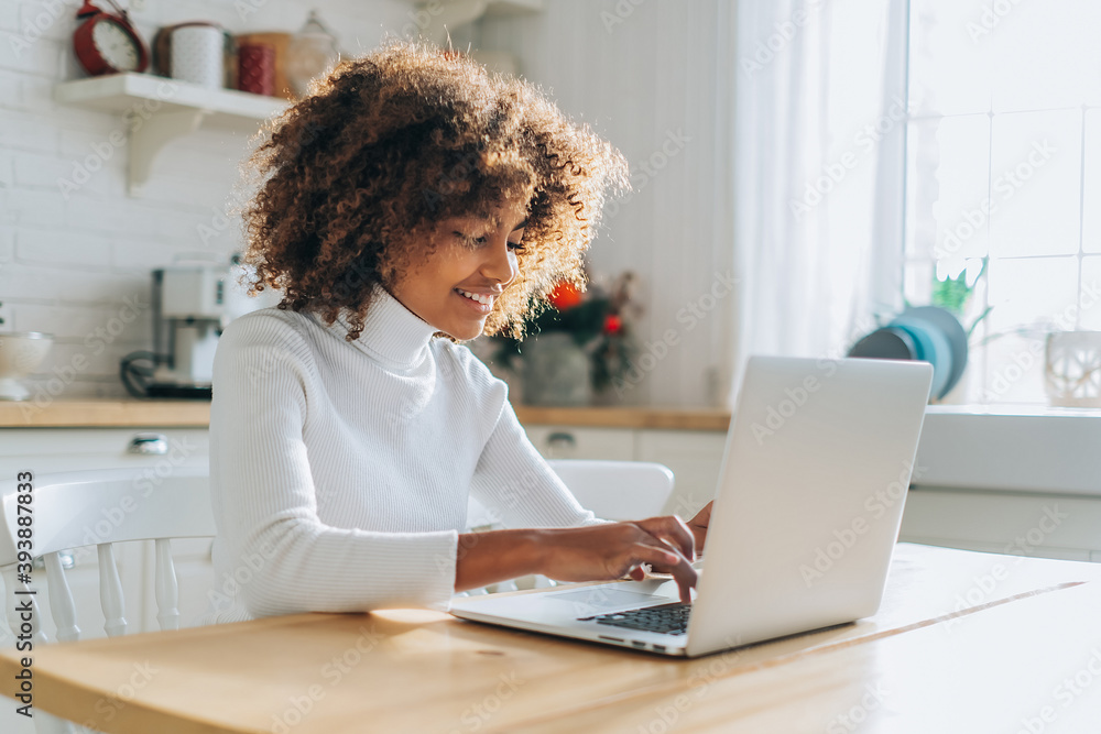 Concentrated and excited dark skinned young buyer with trendy hair looks in laptop smiles and enjoys online shopping closeup